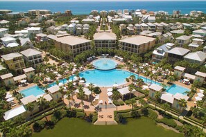 Oversigtsbillede af et resort med flere bygninger, en central swimmingpool og palmer.