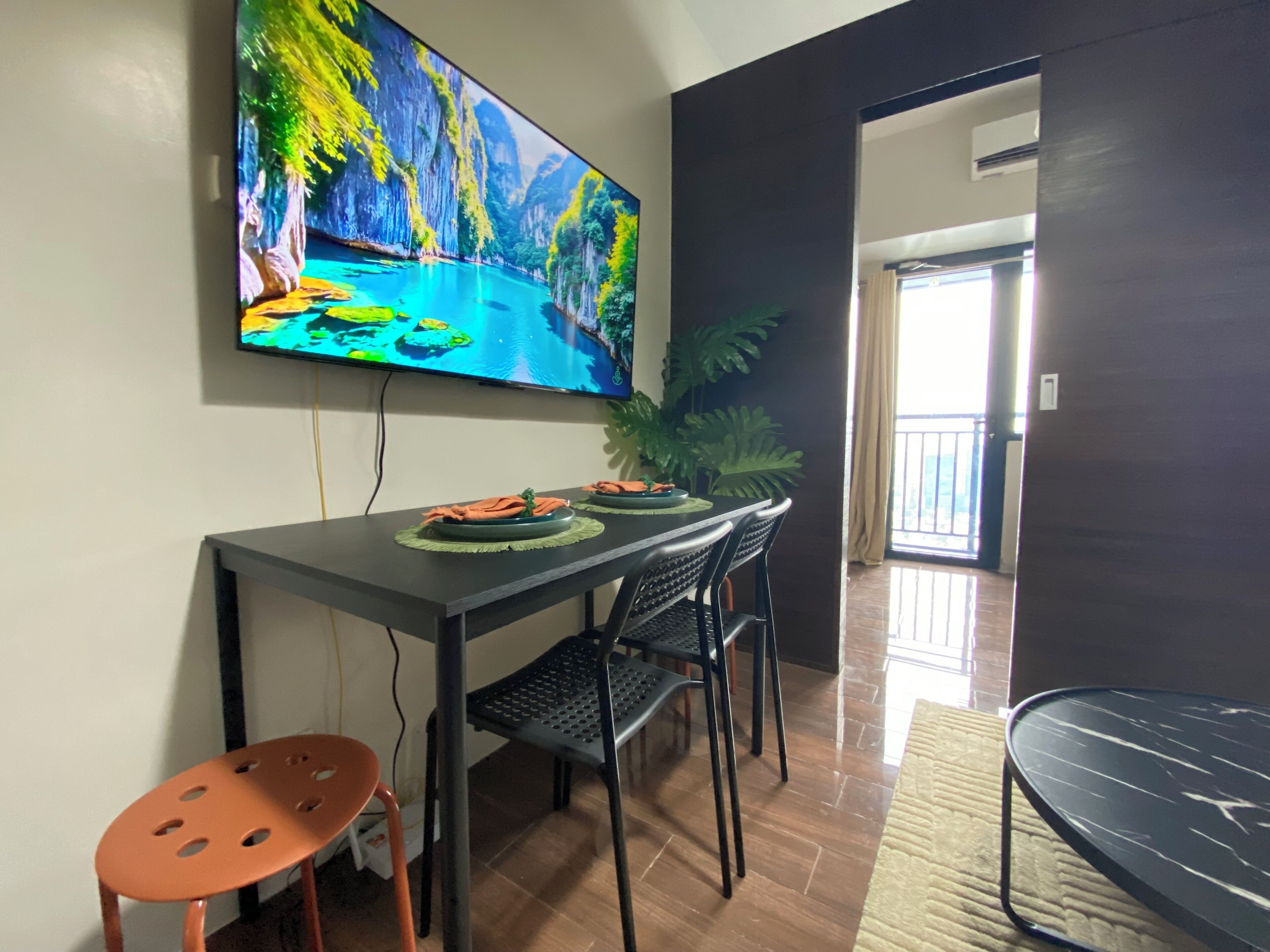Een eethoek met een televisie waarop een mooi landschap te zien is, een tafel met borden en servetten, twee stoelen en een potplant.