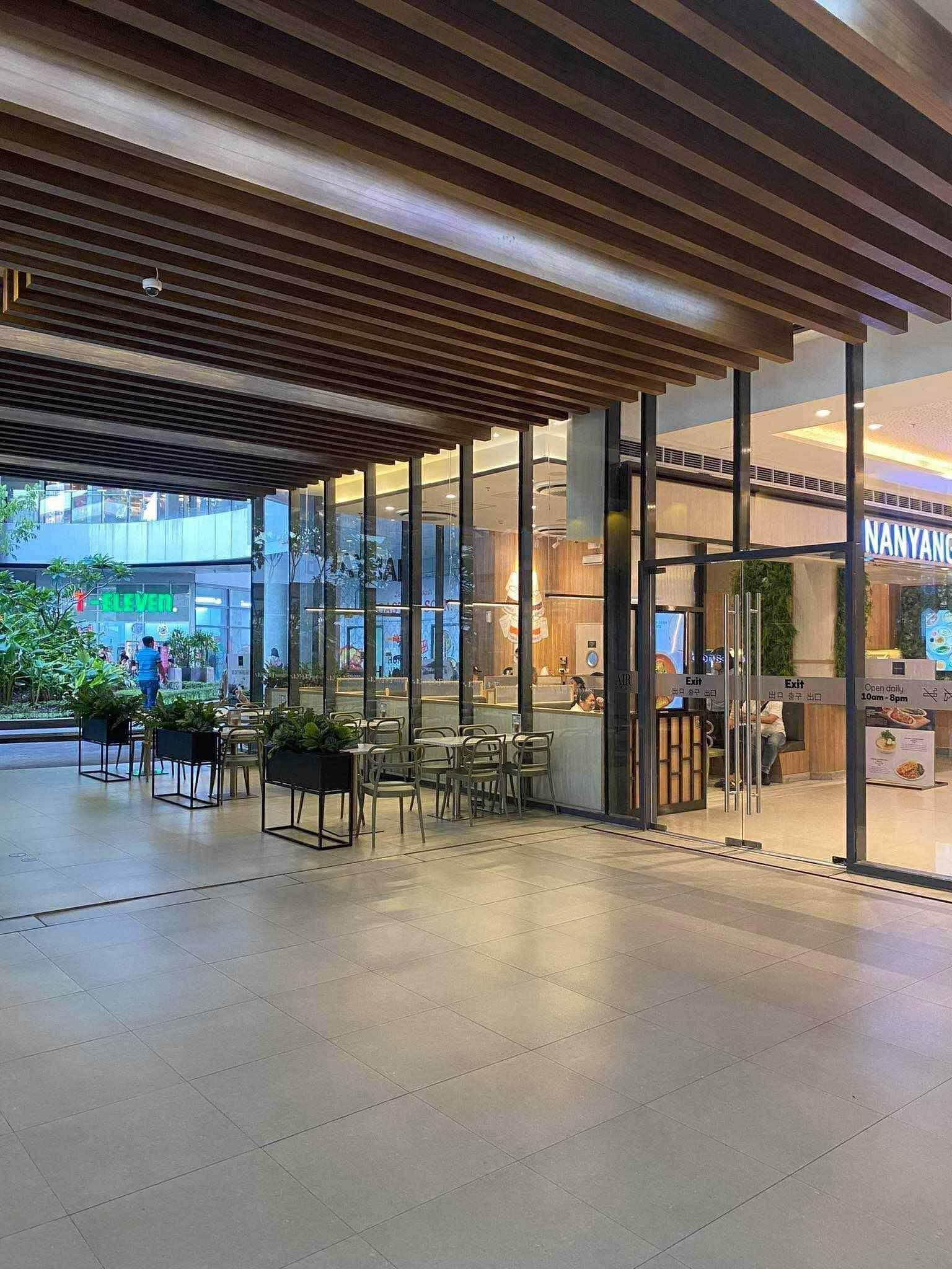 A modern indoor space with a wooden ceiling, glass walls, and a seating area with tables and chairs.