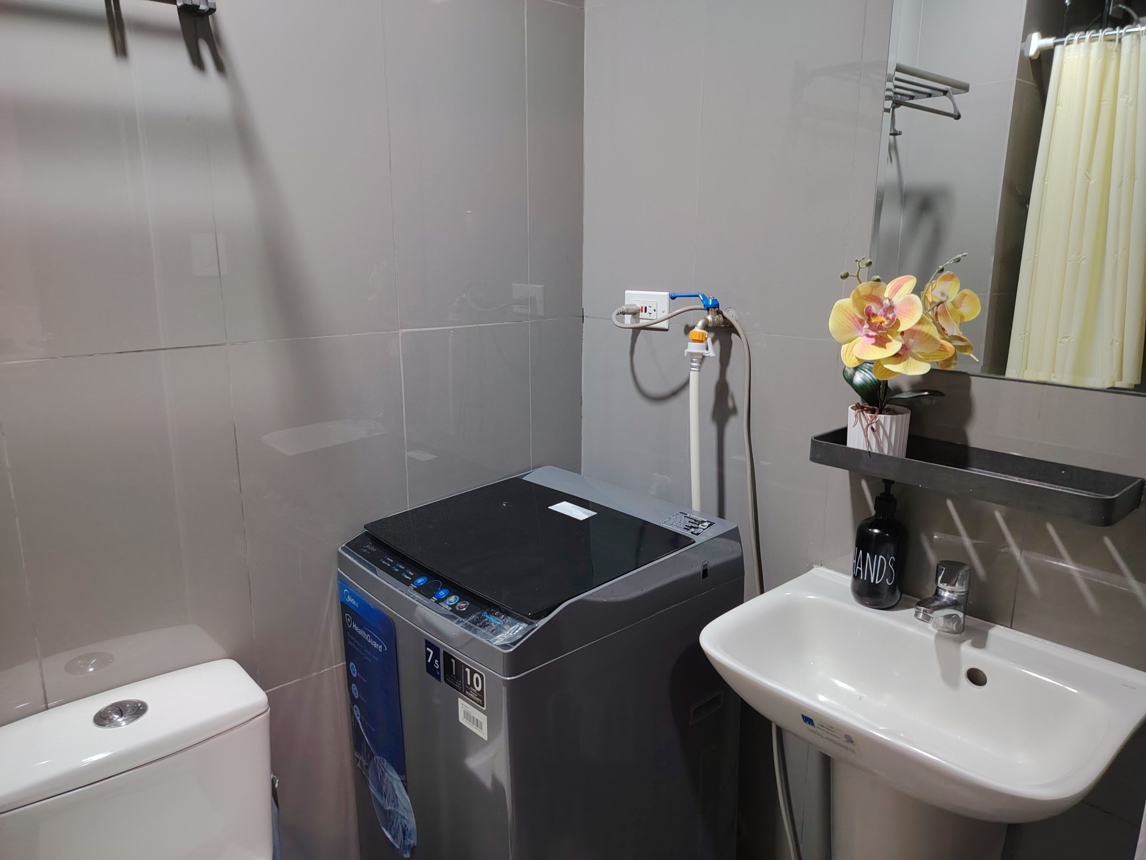 Une salle de bain comprenant des toilettes, un chauffe-eau noir, un lavabo blanc, un miroir et un rideau de douche.
