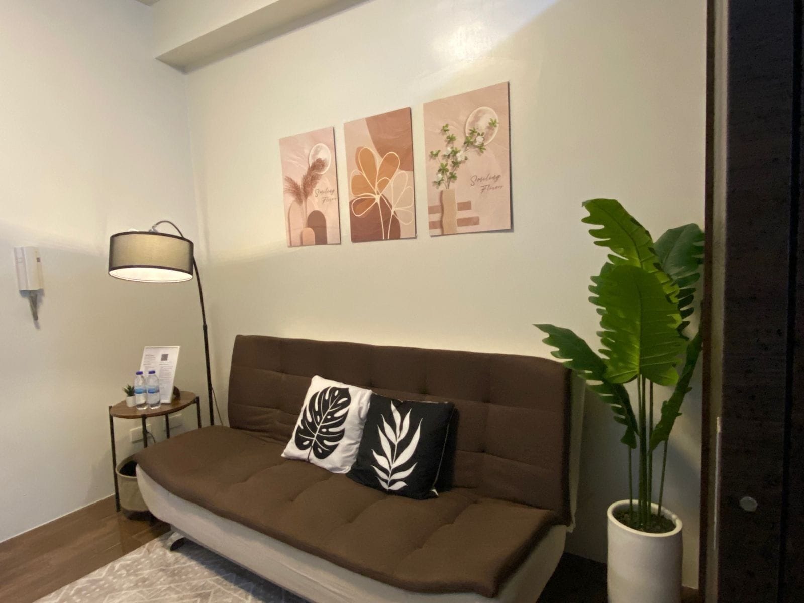 A modern living room with a brown sofa, two decorative pillows, a floor lamp, and a large potted plant.
