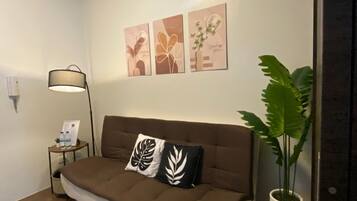 A modern living room with a brown sofa, two decorative pillows, a floor lamp, and a large potted plant.