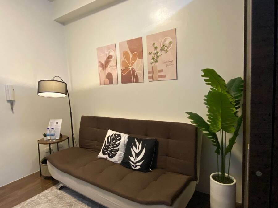 A modern living room with a brown sofa, two decorative pillows, a floor lamp, and a large potted plant.
