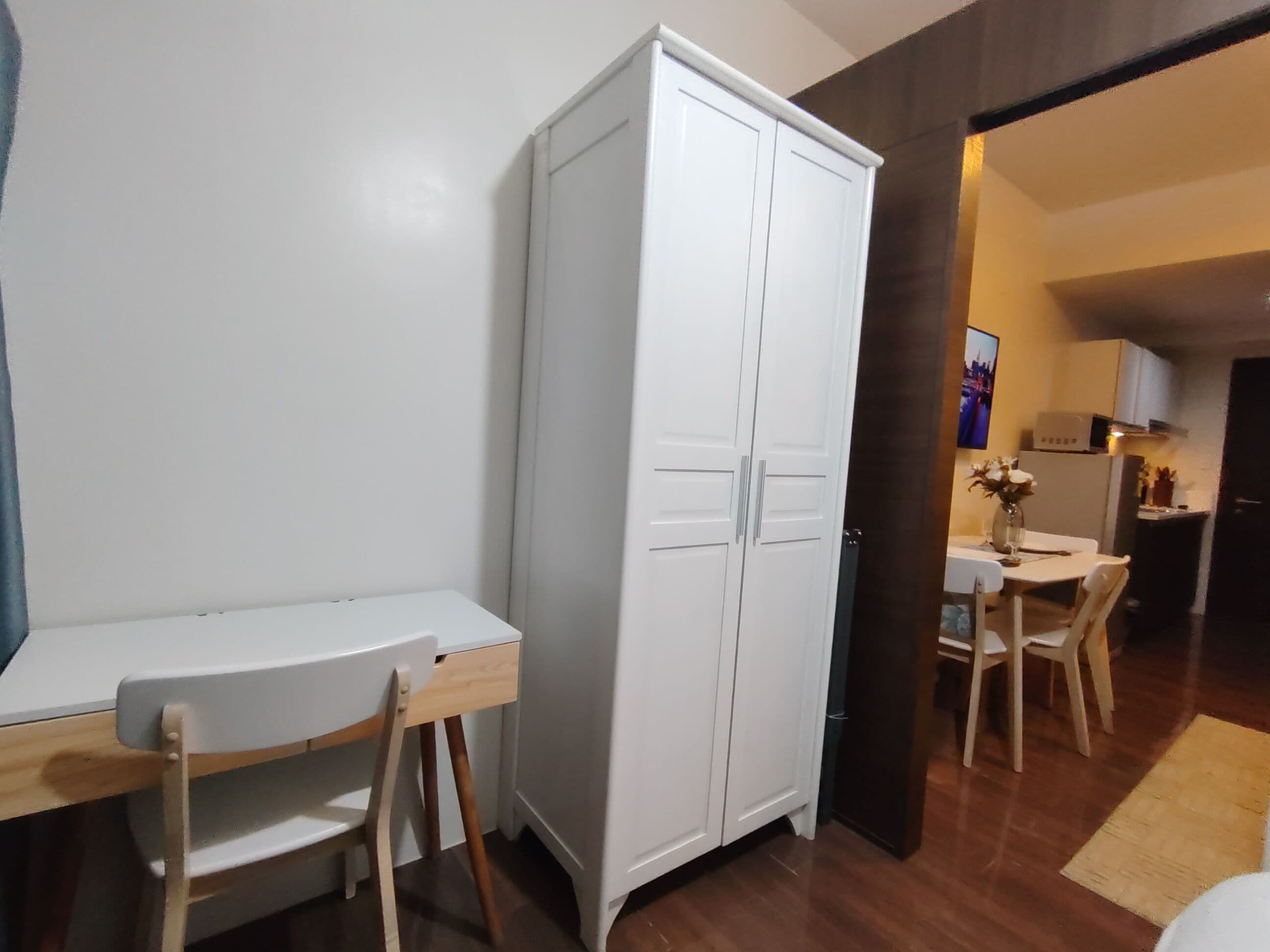 Una habitación con un armario blanco, una pequeña mesa de comedor con sillas, y una cocina visible al fondo.