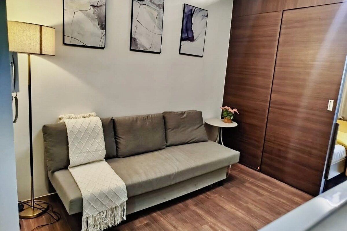 A modern living room with a sofa, a lamp, a small table with a plant, and abstract art on the wall.