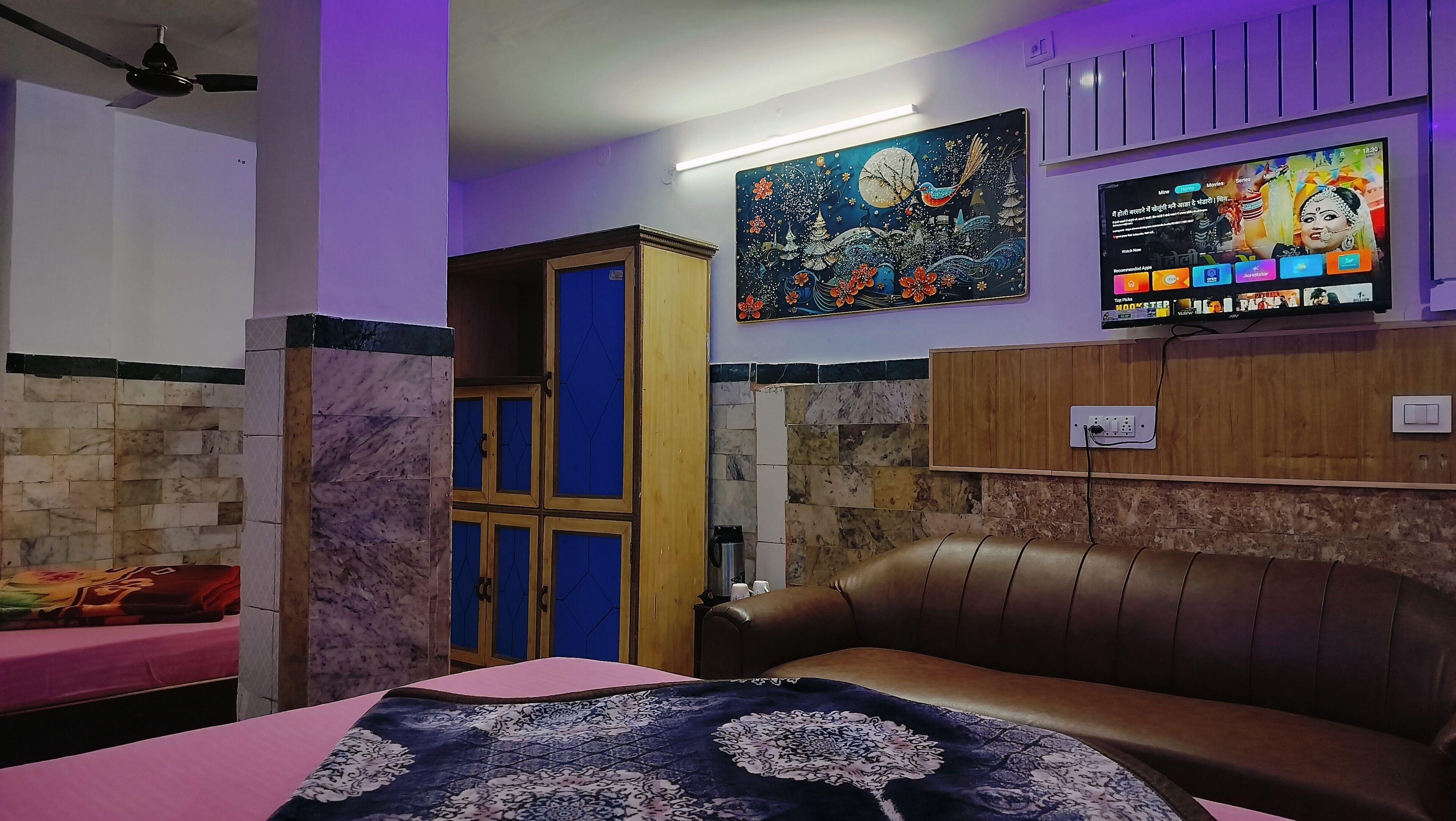 A room with a bed, a couch, a TV, and a wall with a painting.