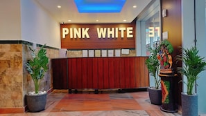Ett entréområde med en träpanel där texten ”ROSA VITT” är skriven med stora bokstäver, en röd panel bakom den och krukväxter på var sin sida.