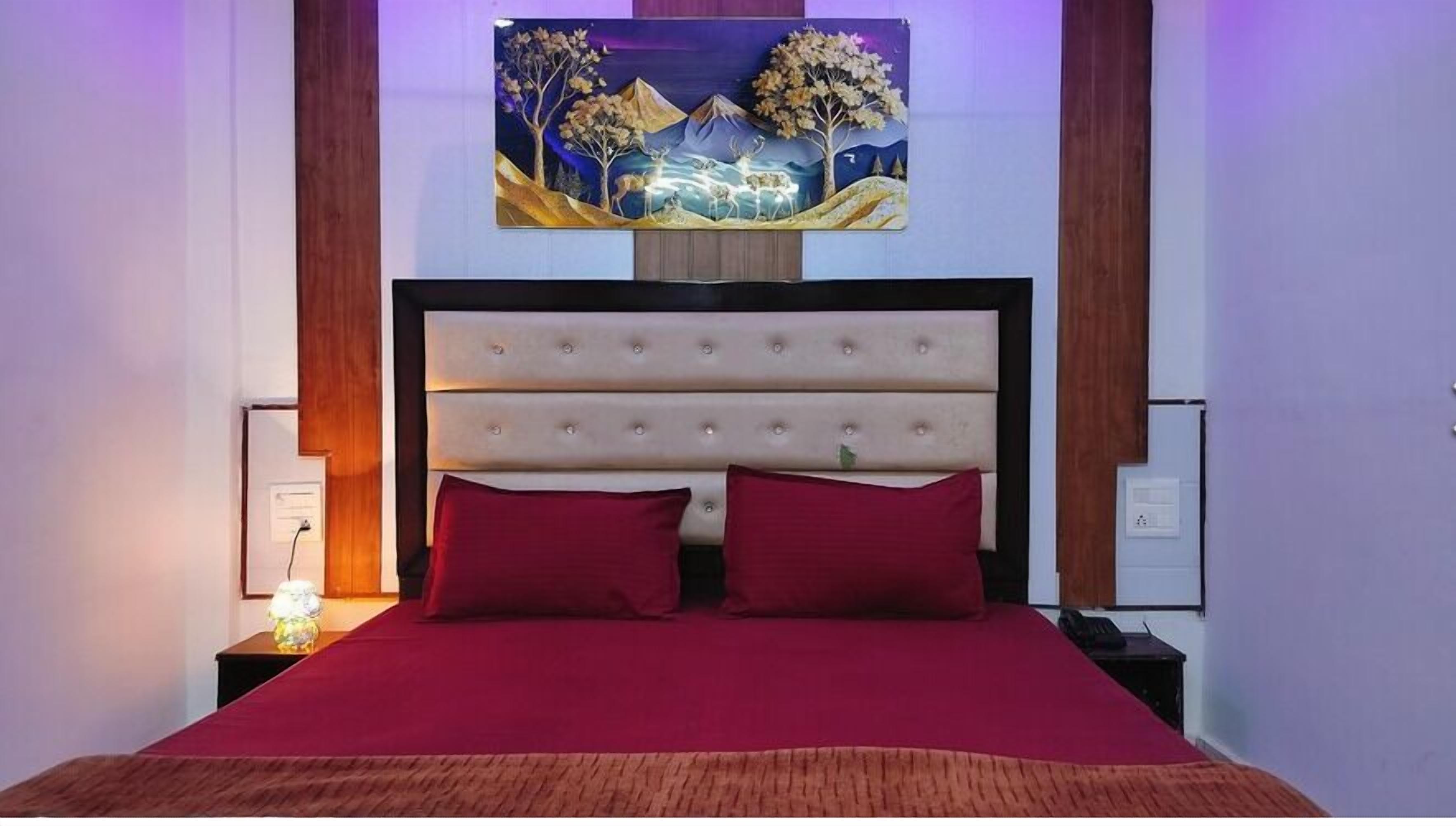 A bed with a red bedspread, a tufted headboard, and a painting above the bed.