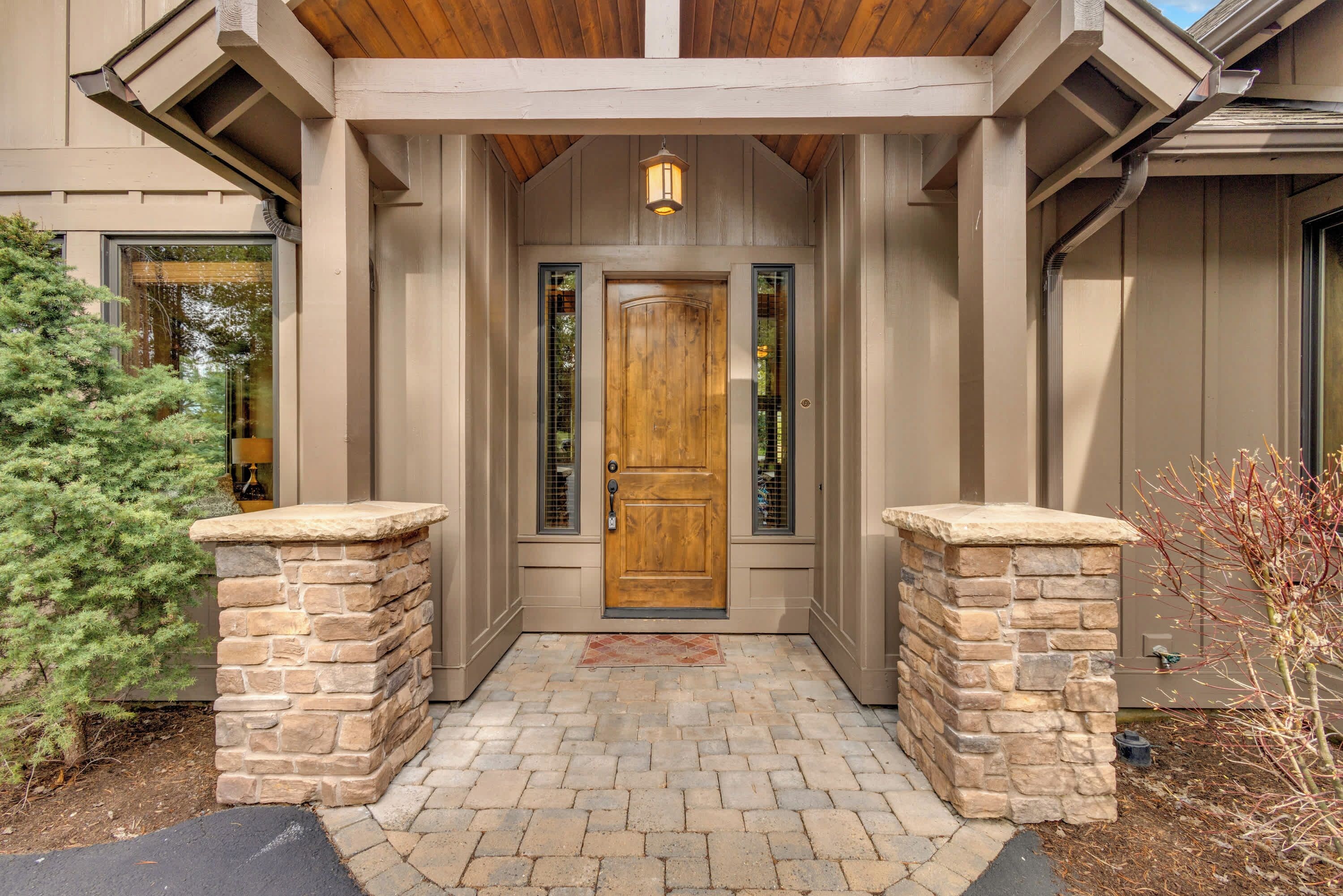 A house entrance with a wooden door, stone pillars, and a brick pathway.