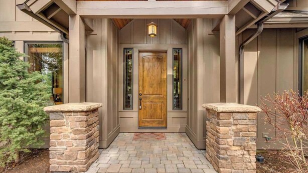 Une entrée de maison avec une porte en bois, des piliers en pierre et un chemin en briques menant à la porte.