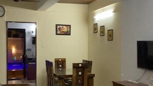 Un salon avec un canapé en cuir marron, une table à manger avec des chaises, un ventilateur de plafond et un téléviseur posé sur un meuble en bois.
