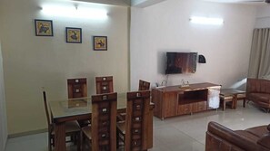 Un comedor con una mesa de vidrio y sillas de madera, un mueble de madera con un televisor, y un sofá de cuero marrón.