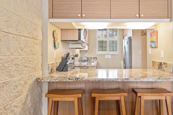 A kitchen with granite countertops, wooden stools, and a view into the dining area. - BEAUTIFUL 2bed/2bath Oceanfront Condo (Maalaea)