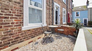 A brick building with a small patio area featuring a table and two chairs, a potted plant, and a gravel ground.
