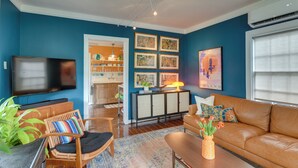 Una sala de estar con pared azul, sofá de cuero marrón, un mueble de madera, televisión y una zona de comedor con mesa y sillas.