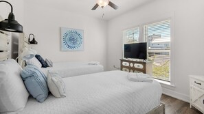 A bedroom with two beds, a ceiling fan, a TV, and a window with blinds. - Beautiful Coastal Chic Home for 9 + Neighborhood Pool in Panama City Beach (Panama City Beach)