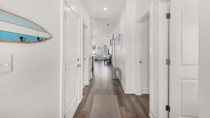A hallway with white walls, wooden flooring, and a surfboard decoration on the left wall. - Beautiful Coastal Chic Home for 9 + Neighborhood Pool in Panama City Beach (Panama City Beach)