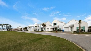 A row of white single-story houses with green shutters, a clear blue sky, and a grassy area in the foreground. - Beautiful Coastal Chic Home for 9 + Neighborhood Pool in Panama City Beach (Panama City Beach)