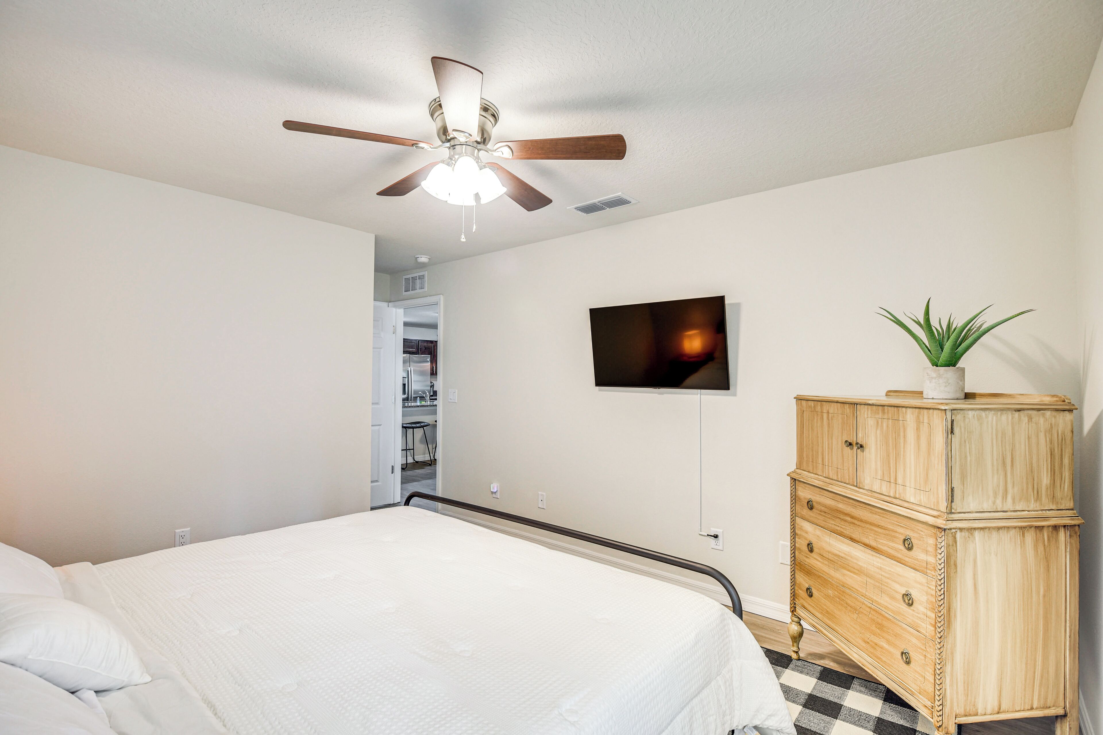 A bedroom with a bed, a ceiling fan, a TV, and a wooden dresser.