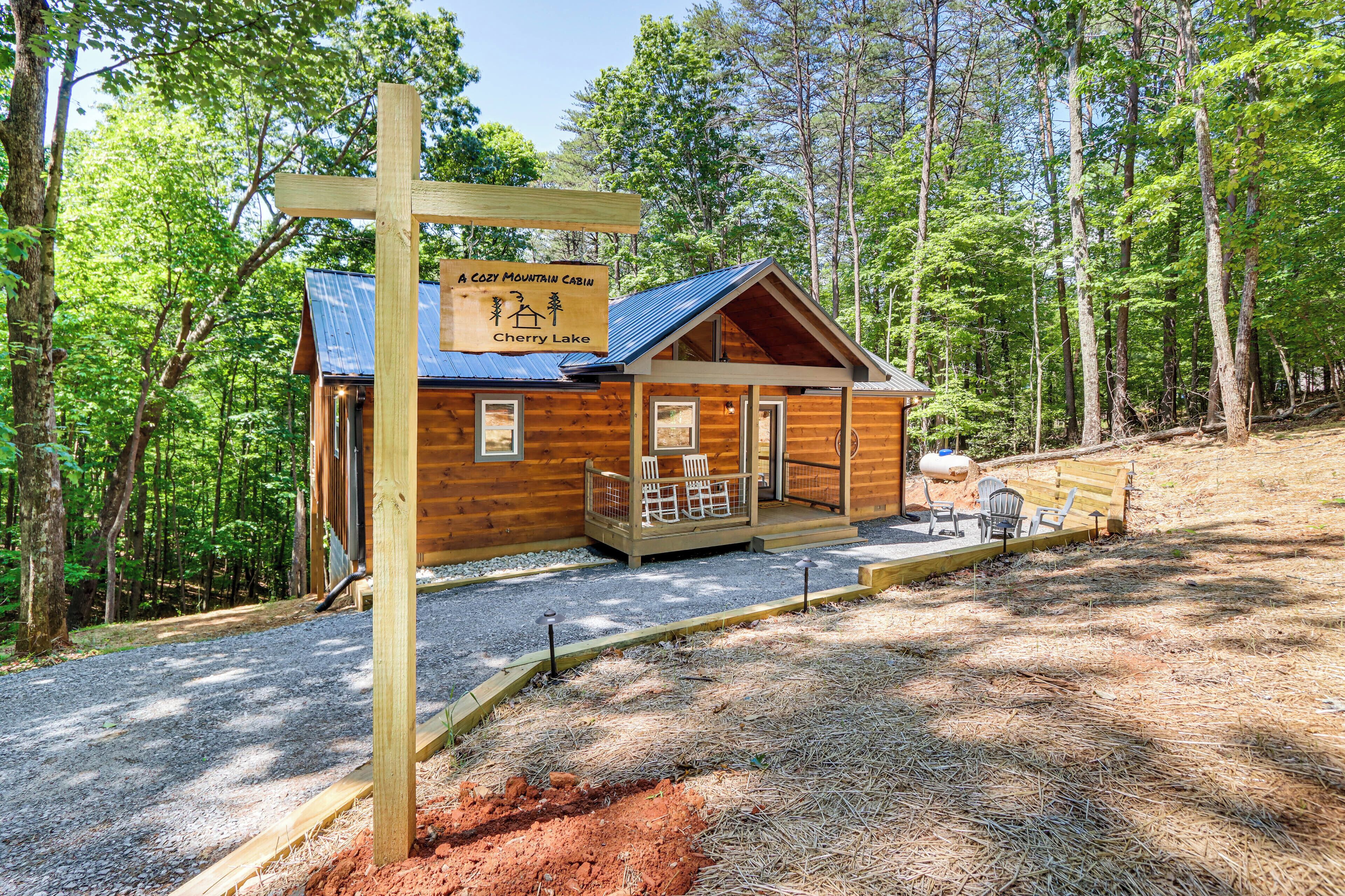 A cozy mountain cabin with a wooden exterior, a porch with chairs, and a sign indicating its name and location.