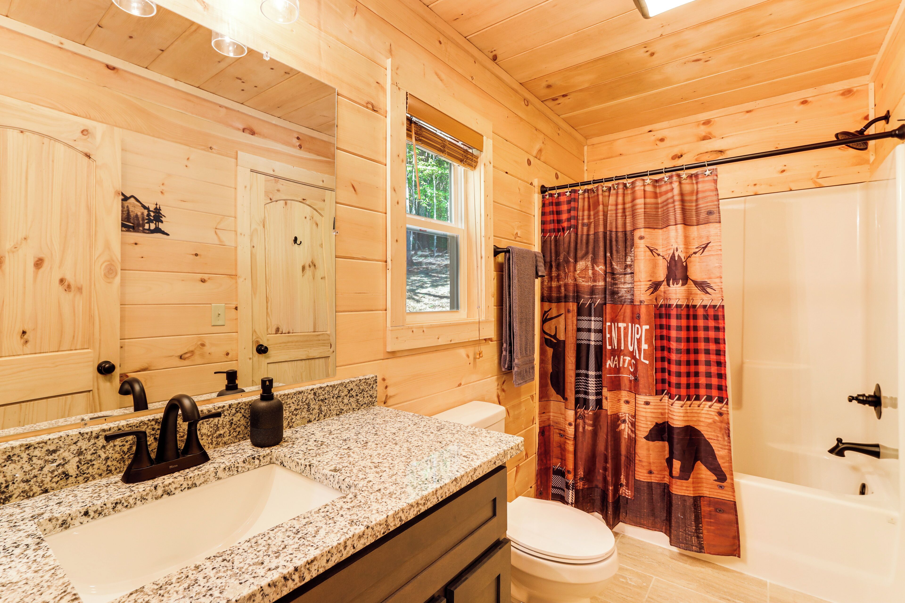 A wooden cabin bathroom with a granite sink, a toilet, and a shower curtain with animal prints.