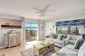 A living room with a sofa, a coffee table, and a view of the beach.