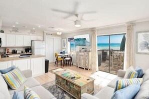 A modern living room with a sofa, coffee table, and a view of the beach through large glass doors.