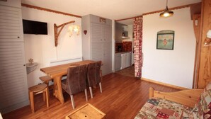 A compact kitchen with wooden cabinets, a dining table with chairs, a small sink, and a television mounted on the wall. - 150m from ski slopes, 2nd floor, view ski slopes, balcony, parking, tv, ski locker, 29m² (Les Saisies)