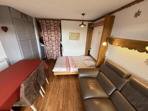 A compact room with a bed, a sofa, a dining table, and a small kitchenette area.