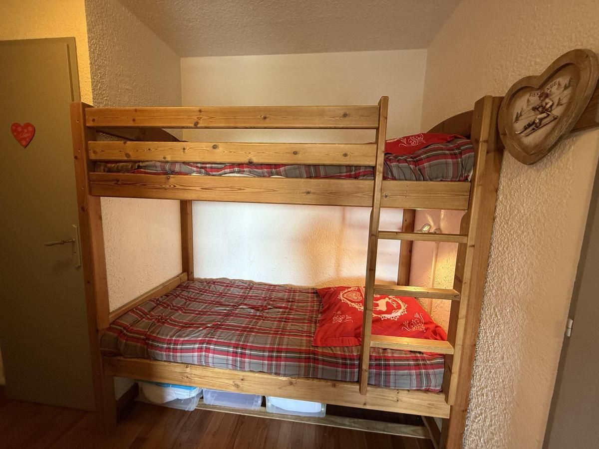 Un lit superposé avec une couvre-lit à carreaux et des oreillers rouges, une échelle et une horloge en forme de cœur accrochée au mur.