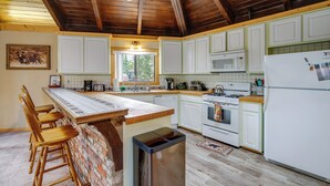 A kitchen with white cabinets, a wooden ceiling, and a brick accent wall. - Big Bear Cabin w/ Hot Tub < 3 Mi to Skiing! (Big Bear City)