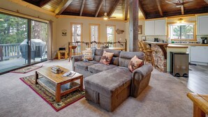 A spacious living room with a large sectional sofa, a wooden coffee table, and a dining area with a kitchen in the background. - Big Bear Cabin w/ Hot Tub < 3 Mi to Skiing! (Big Bear City)