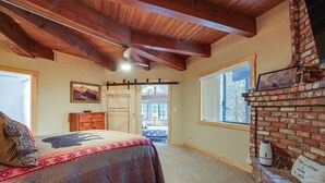 A bedroom with a bed, a wooden dresser, a brick fireplace, and a window. - Big Bear Cabin w/ Hot Tub < 3 Mi to Skiing! (Big Bear City)