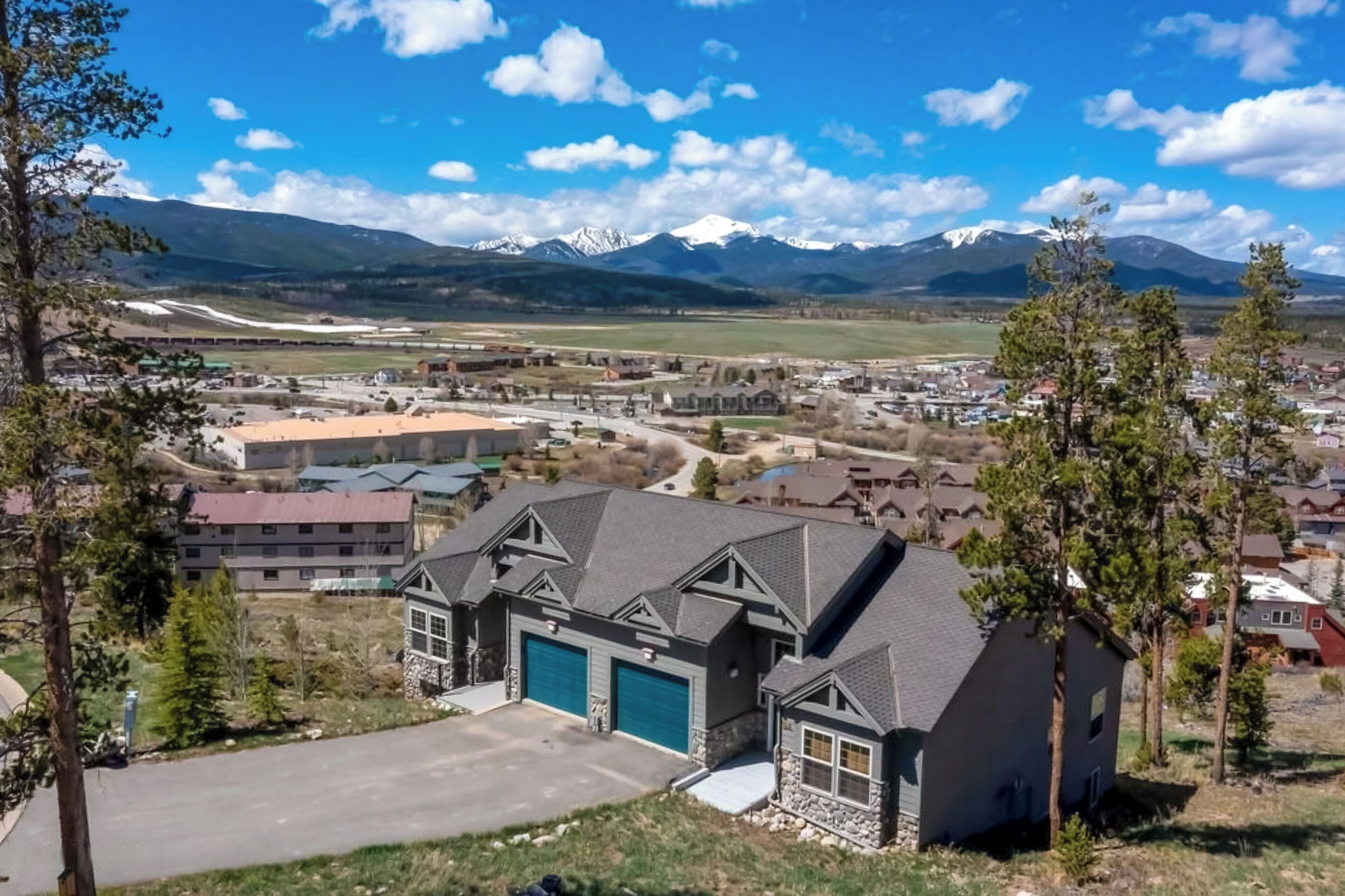 Un barrio residencial con casas, un edificio grande con garaje y montañas nevadas al fondo.