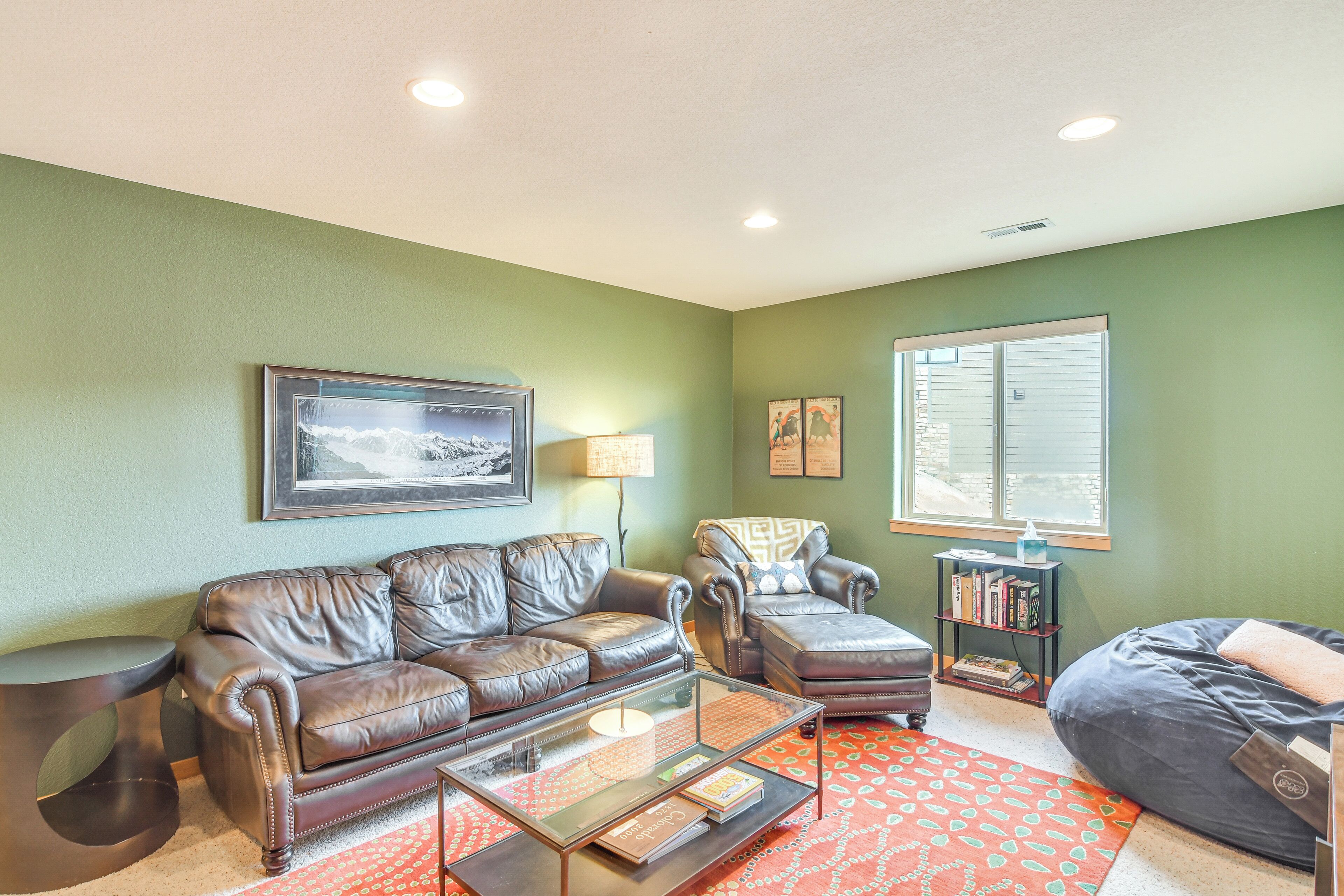 A living room with a brown leather sofa, a glass coffee table, a patterned rug, and a window with blinds.