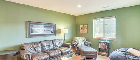 A living room with a brown leather sofa, a glass coffee table, a patterned rug, and a window with blinds.