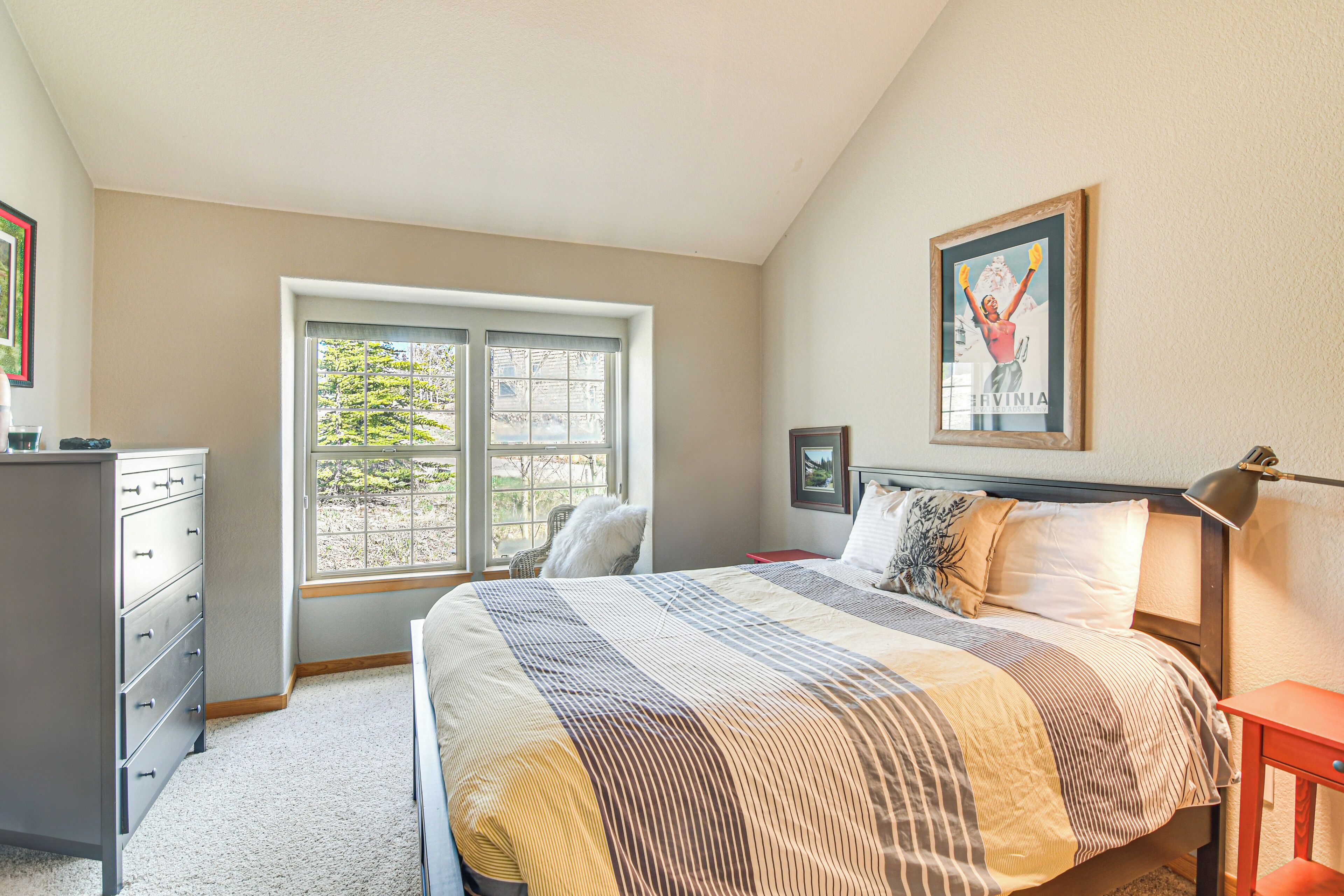A bedroom with a large bed, a dresser, a window, and a framed picture on the wall.