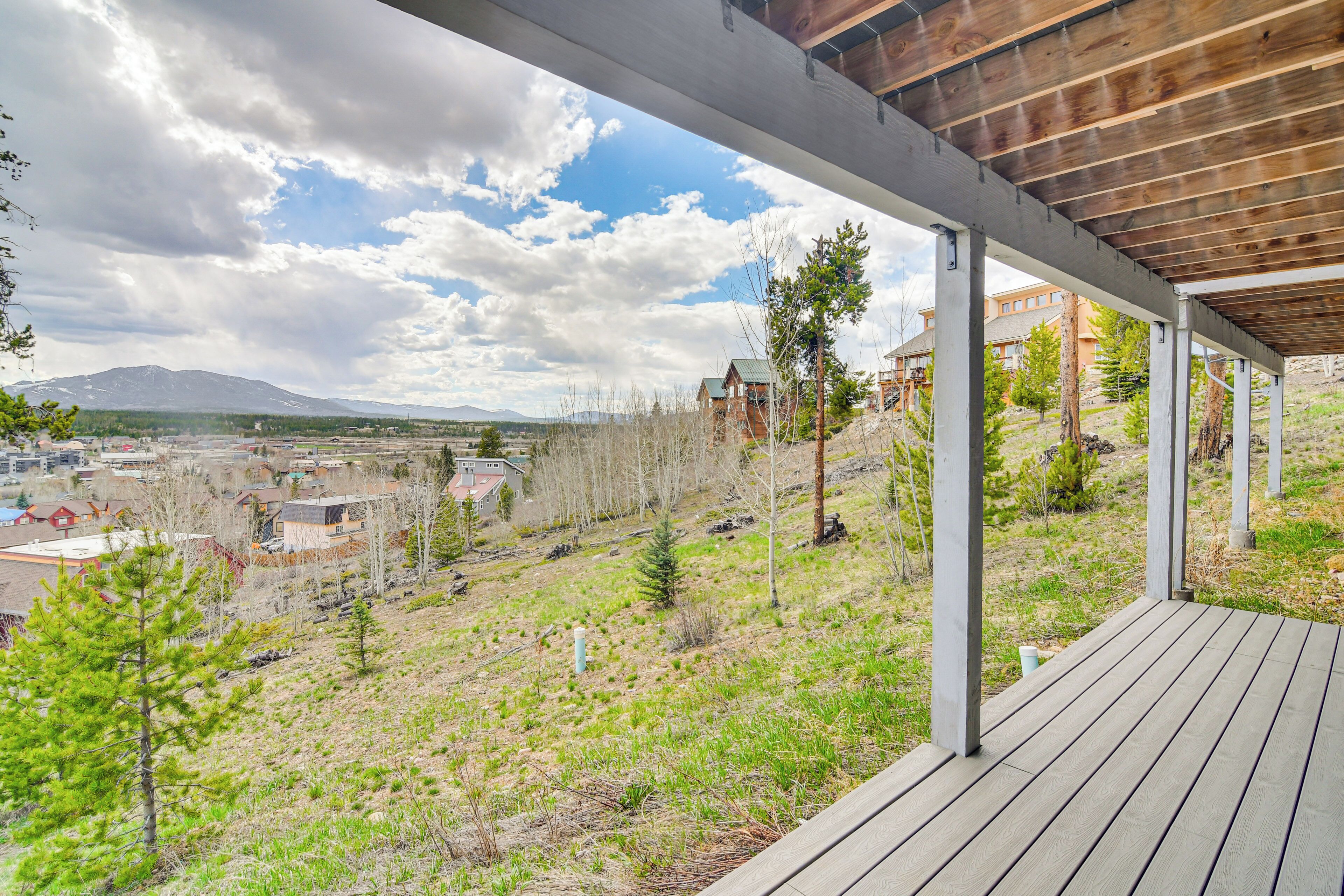 A covered outdoor area with a view of a mountainous landscape, wooden deck, and a grassy hill with scattered trees.
