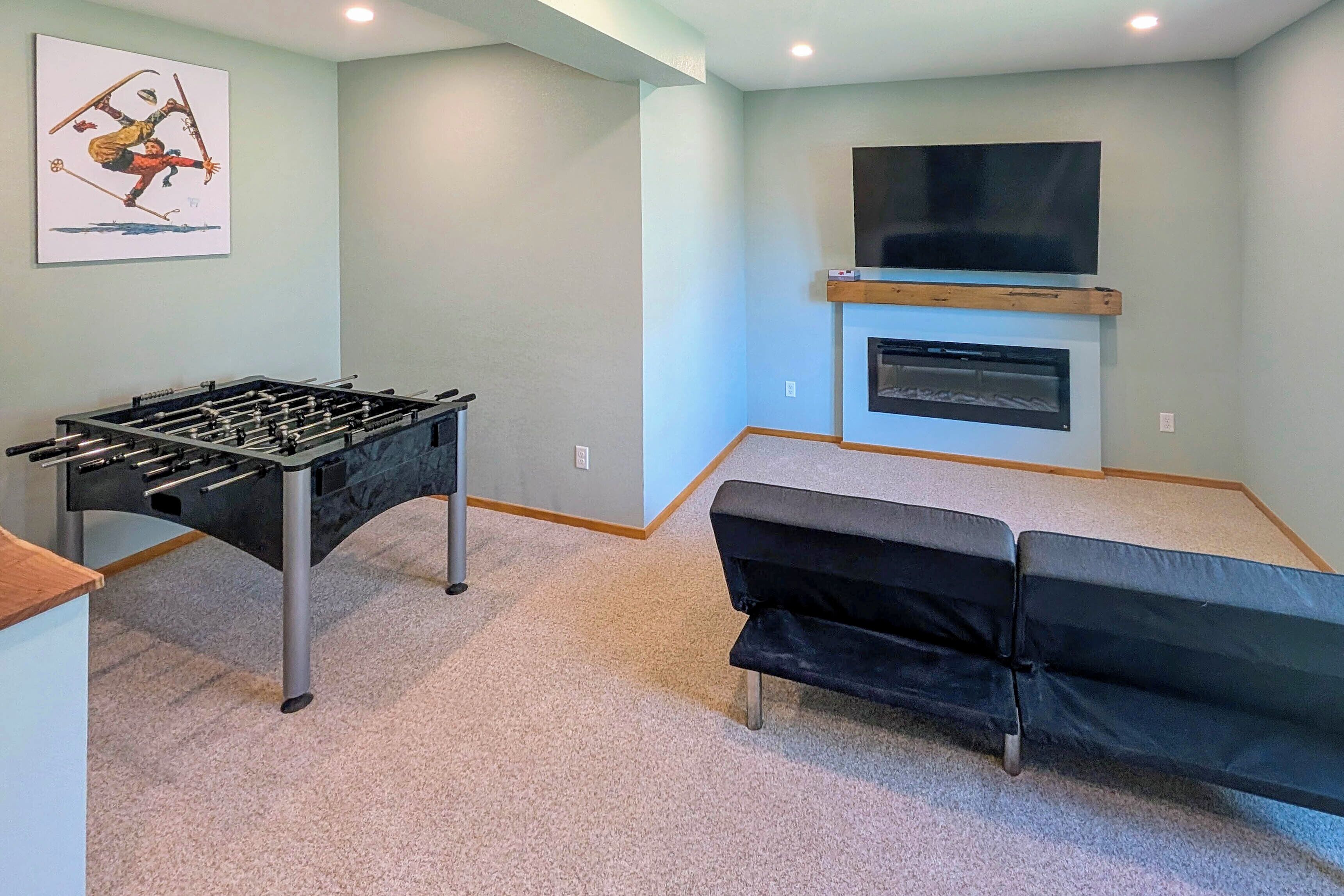 A room with a foosball table, a flat-screen TV mounted above a fireplace, and a sofa.