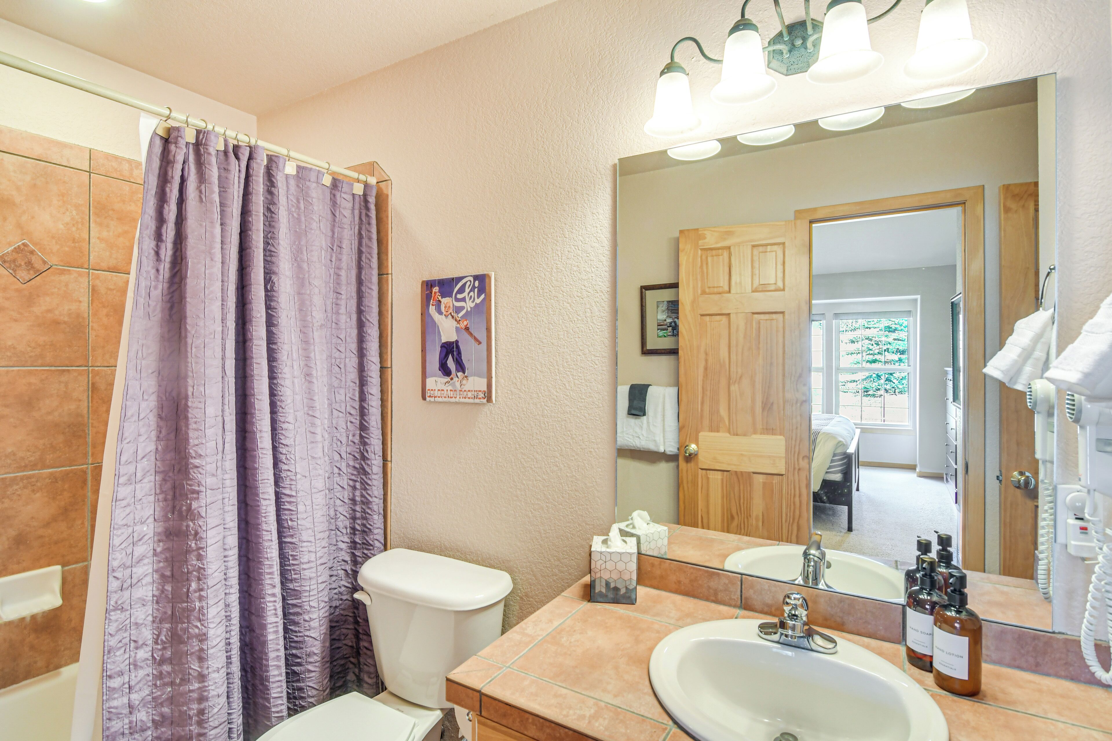 A bathroom with a shower curtain, toilet, sink, and mirror.