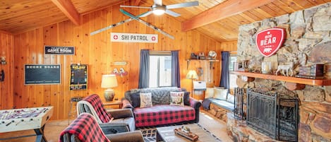 A cozy lodge interior with a game room, sofa, fireplace, and wooden decor.