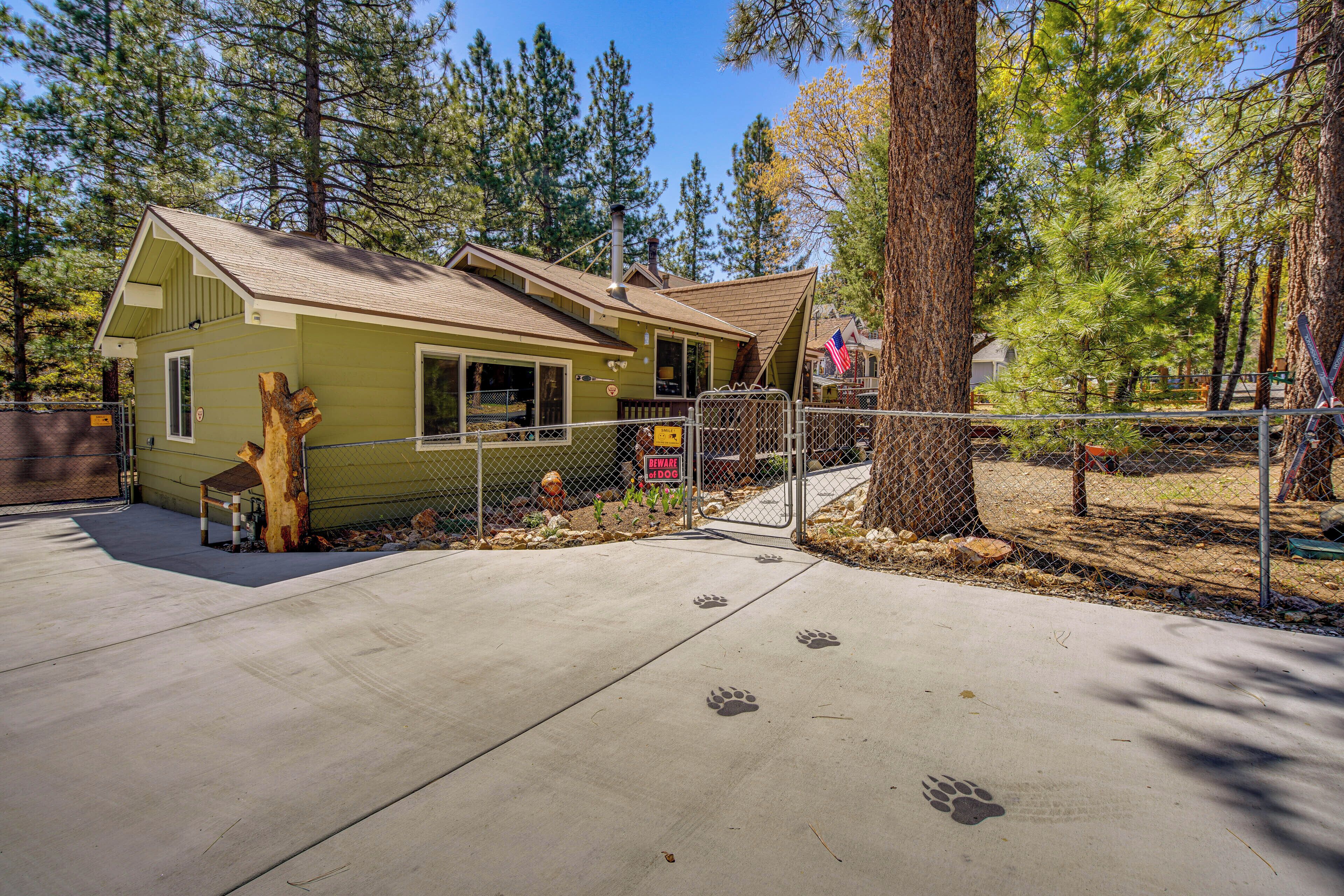 A small, single-story house with a sloped roof, a fenced yard, and a concrete driveway.