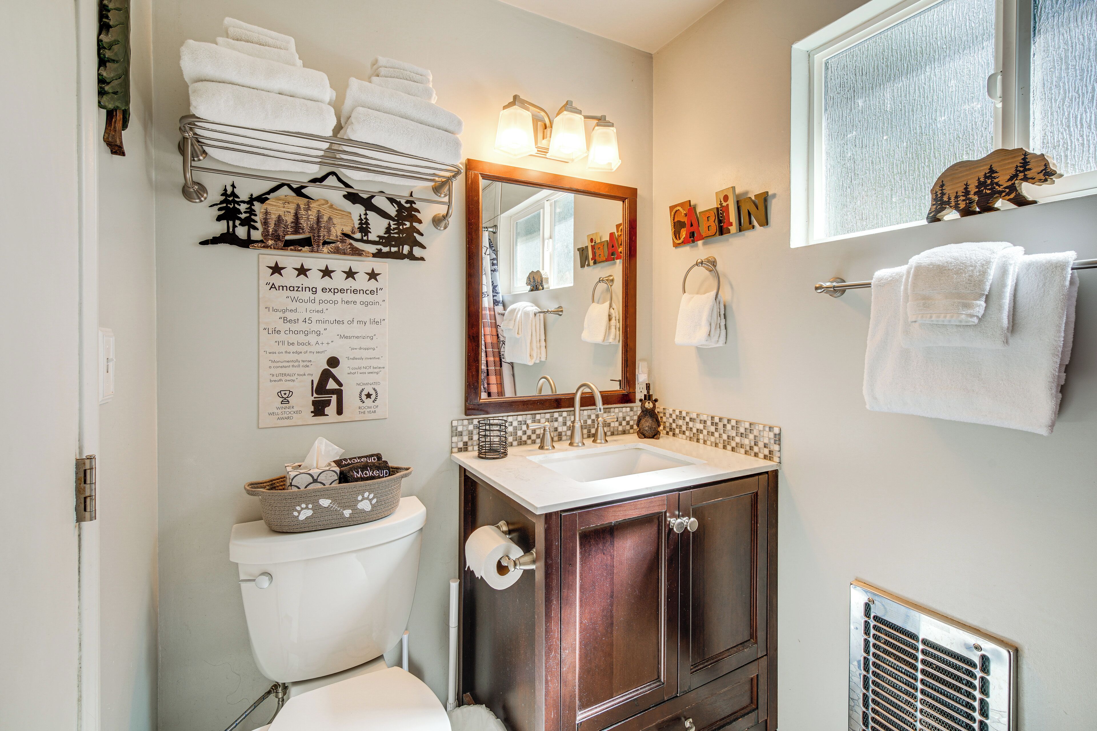 A bathroom with a toilet, sink, and mirror. There are towels on the wall and a basket of toiletries on the toilet.