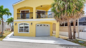 Una casa amarilla de dos pisos con garaje, balcón y una palmera.