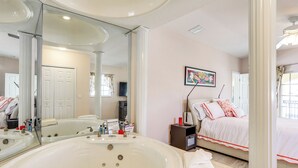 Un baño moderno con una bañera grande, un espejo y una mesita de noche con lámpara.
