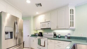 Una cocina con gabinetes blancos, electrodomésticos de acero inoxidable y encimera verde.