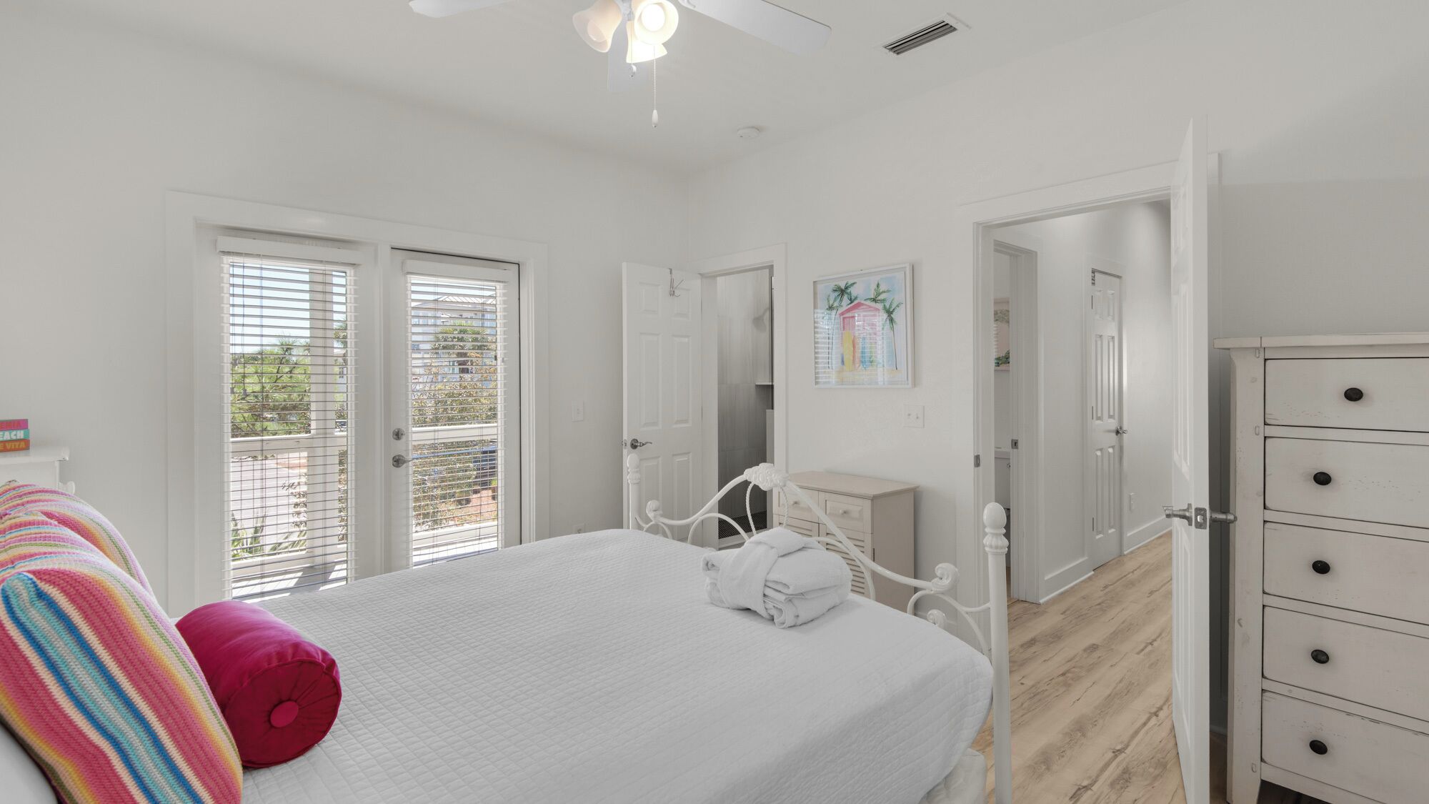 A bedroom with a bed, a dresser, a painting, and a balcony door.