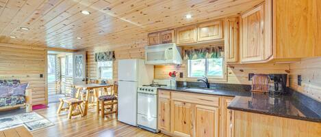 A wooden cabin interior with a kitchen area featuring wooden cabinets, a microwave, a stove, and a refrigerator.