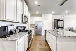 A modern kitchen with white cabinets, stainless steel appliances, granite countertops, and a central island.