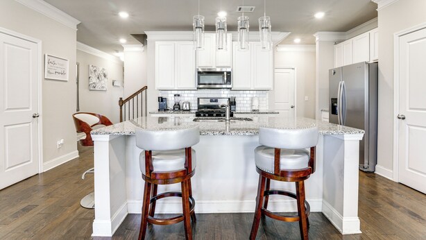 A modern kitchen with white cabinetry, a granite countertop, stainless steel appliances, and a central island with bar stools. - Lawrenceville Townhome w/ Community Pool Access! (Lawrenceville)